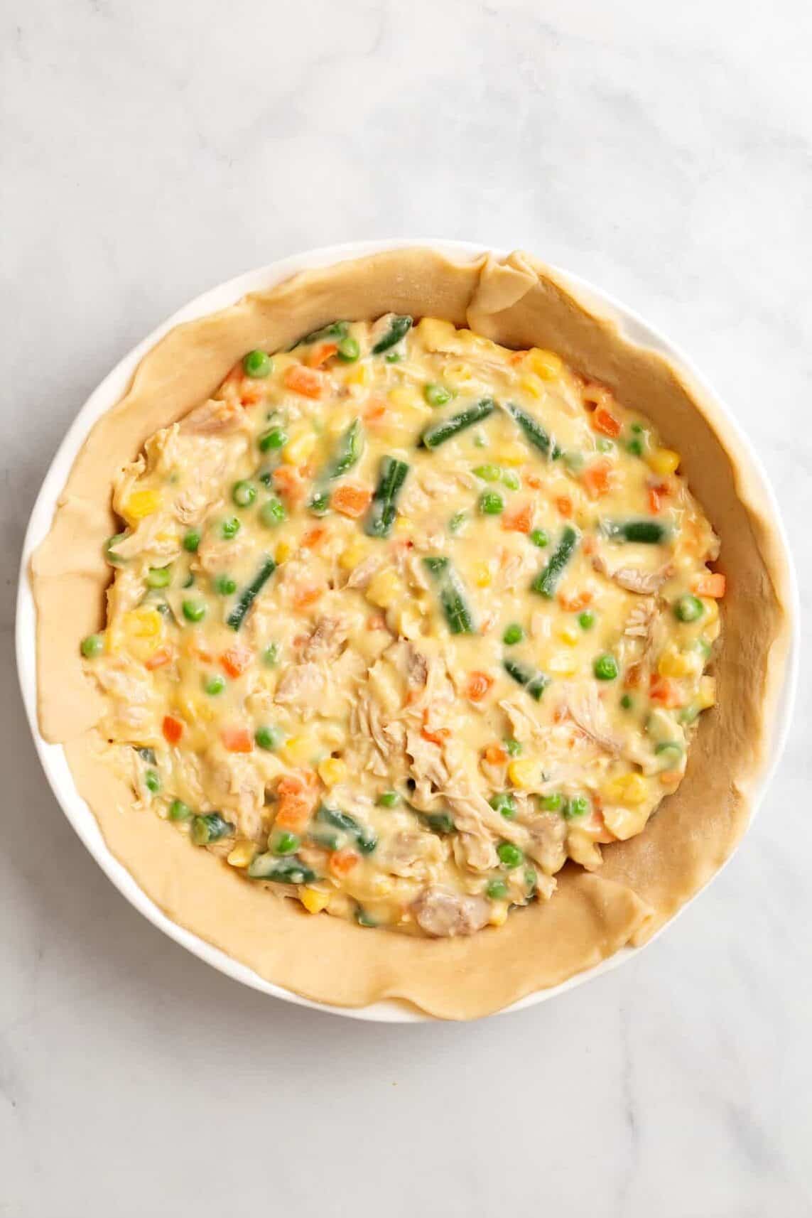 top down image of raw pie crust lined on a pie dish topped with campbell's chicken pot pie filling.
