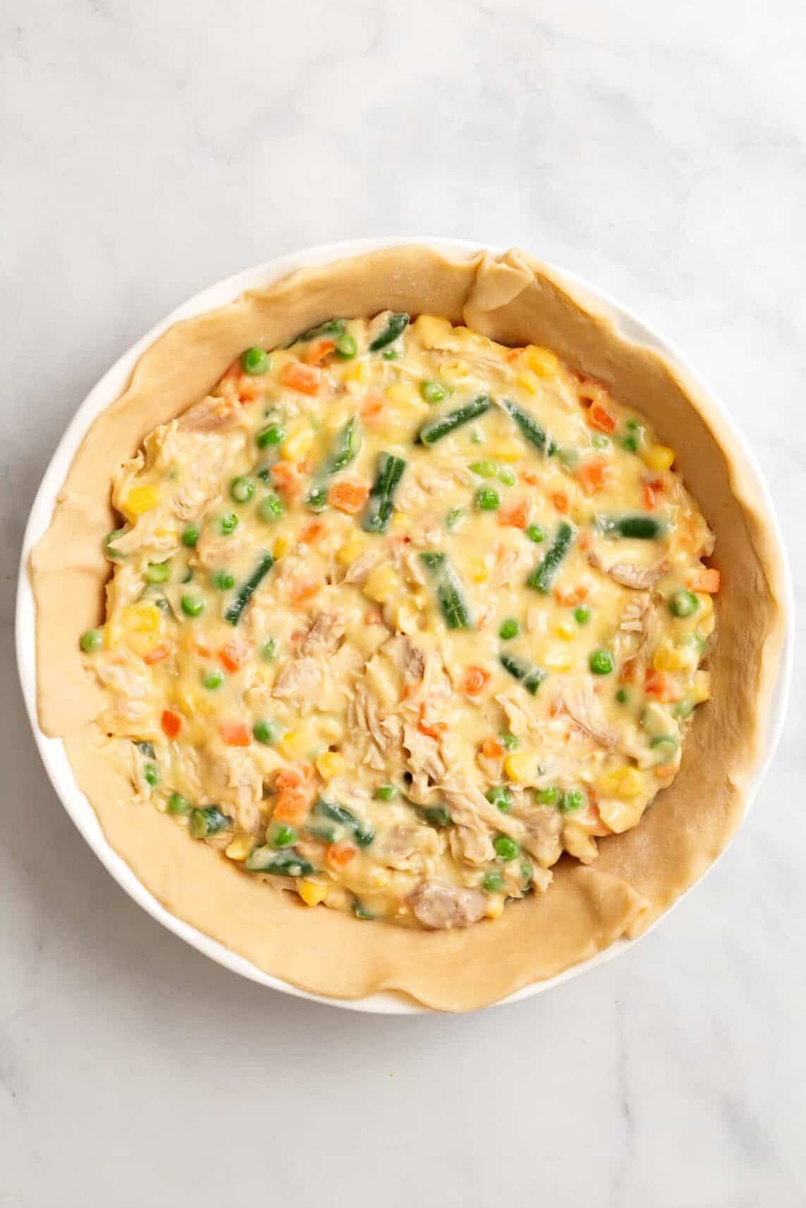 top down image of raw pie crust lined on a pie dish topped with campbell's chicken pot pie filling. 