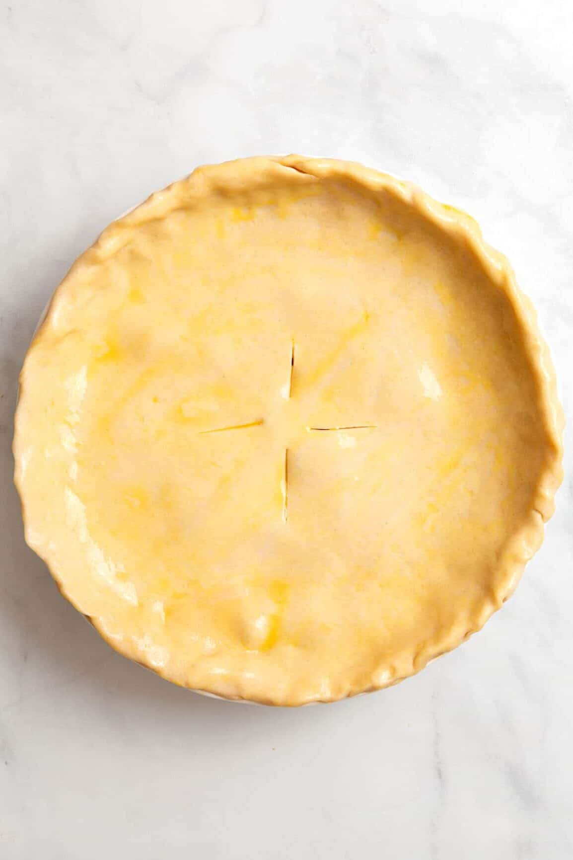 top down image of raw pie crust lined on a pie dish topped with campbell's chicken pot pie filling and topped with the top layer of pie crust. 