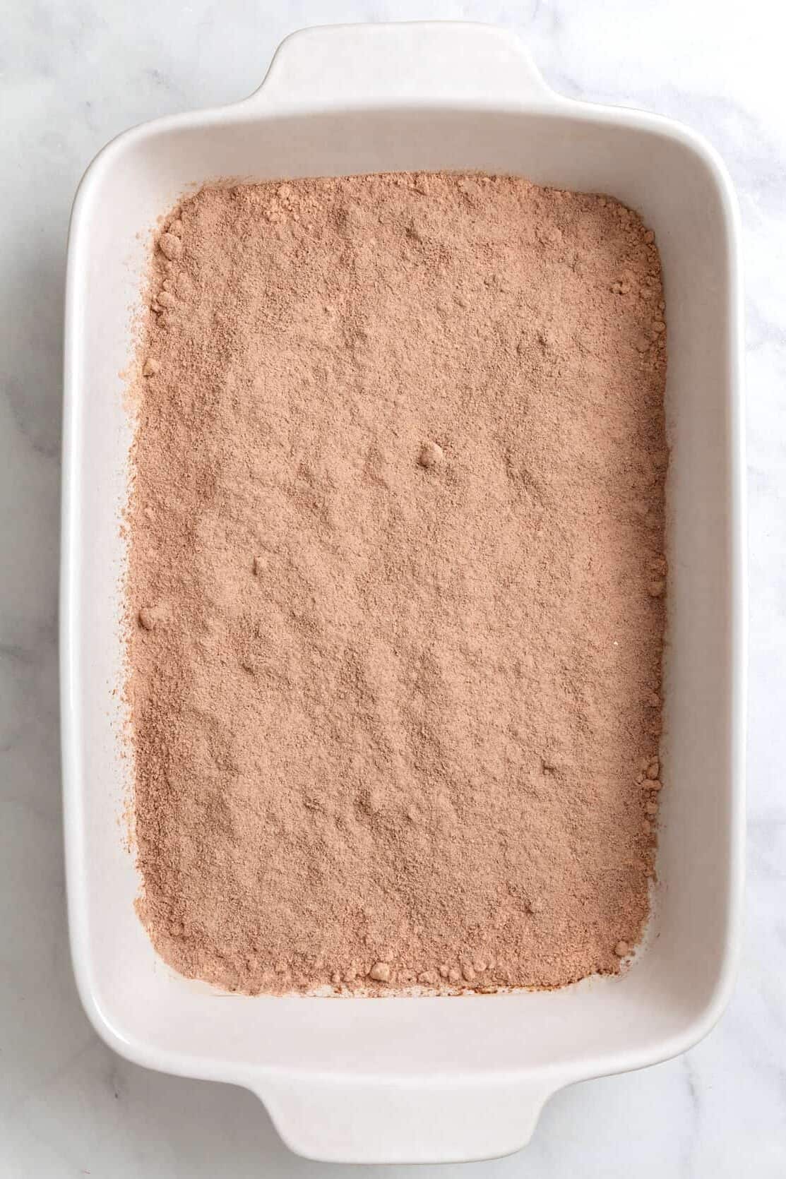top down image of chocolate cake mix layered at the bottom of a 9x13 ceramic baking dish. 