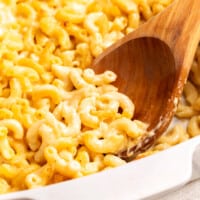 A wooden spoon scooping Cracker Barrel mac and cheese from a baking dish.