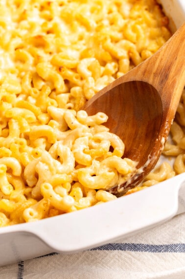 A wooden spoon scooping Cracker Barrel mac and cheese from a baking dish.