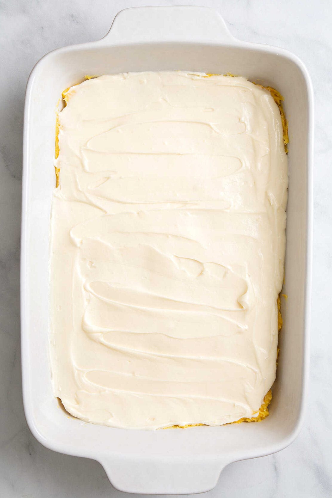 top down image of a 9x13 casserole dish with bake cake box mix topped with powdered sugar and cream cheese frosting.