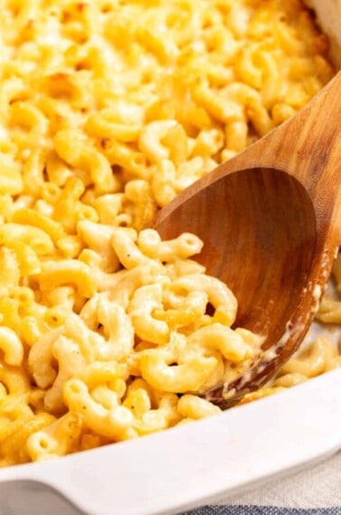 A wooden spoon scooping Cracker Barrel mac and cheese from a baking dish.
