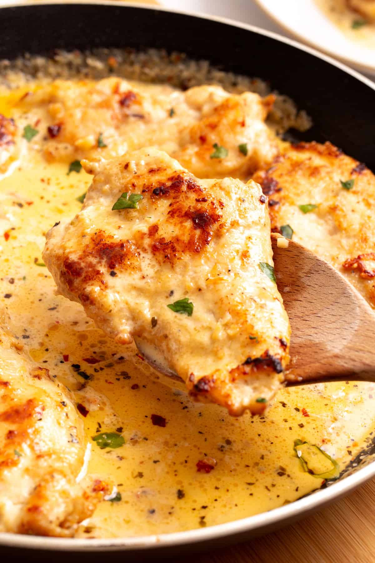 close up image of a marry me chicken tenderloin sitting on a wooden spoon. 