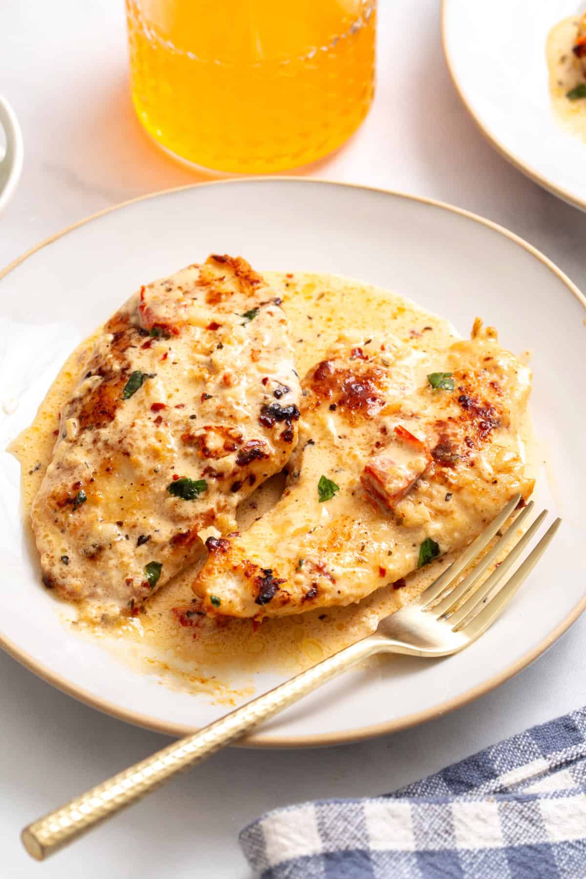 serving of marry me chicken served on a white round plate with a gold fork.