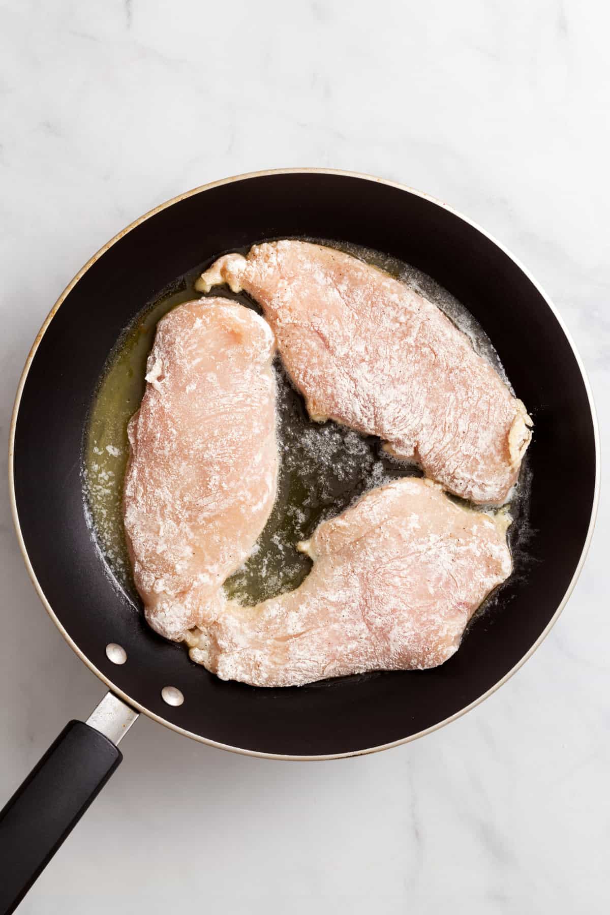 top down image of a skillet with three flour-coated chicken breast.