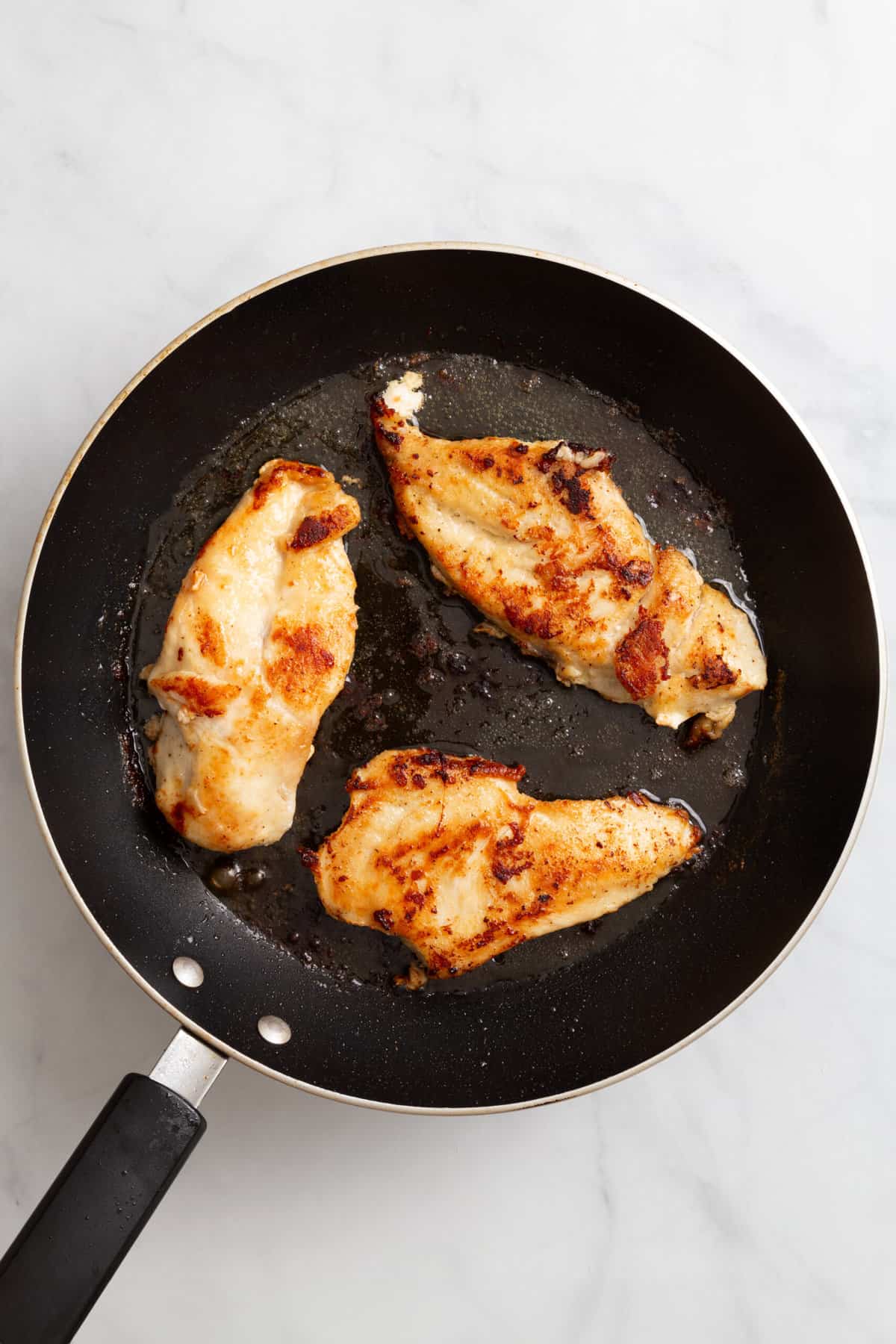 top down image of a skillet with three cooked chicken breast.