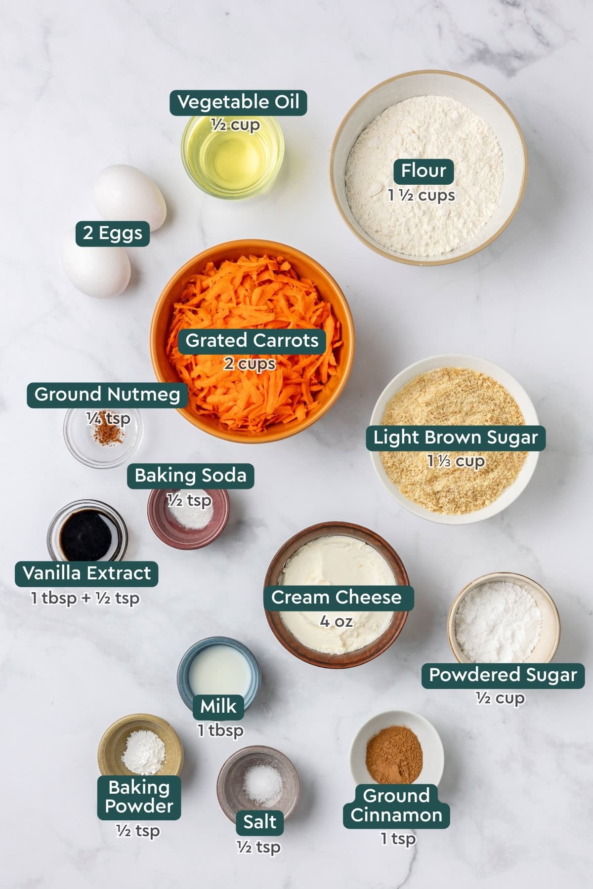 Ingredients for carrot cake muffins, including oil, flour, eggs, carrot, sugar, nutmeg, baking soda, vanilla, cream cheese, powdered sugar, cinnamon, salt, milk, baking powder.
