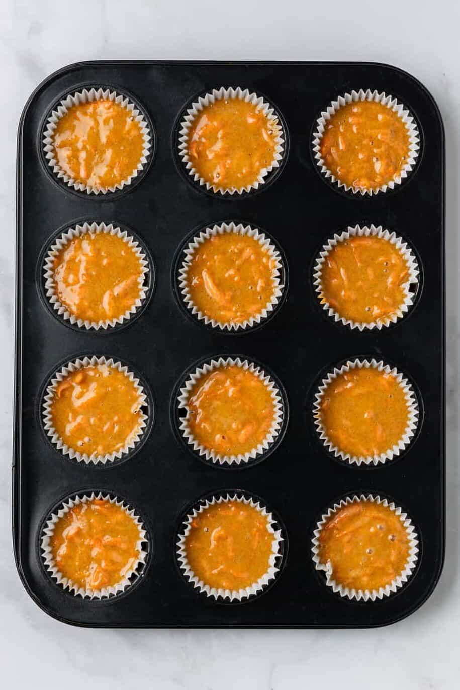 top down image of twelve carrot cake muffin batter prepped in a muffin tin. 