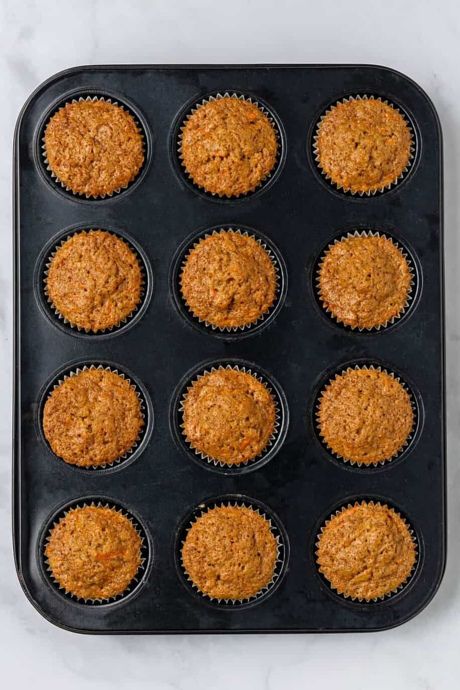 top down image of twelve carrot cake muffins baked in a muffin tin. 