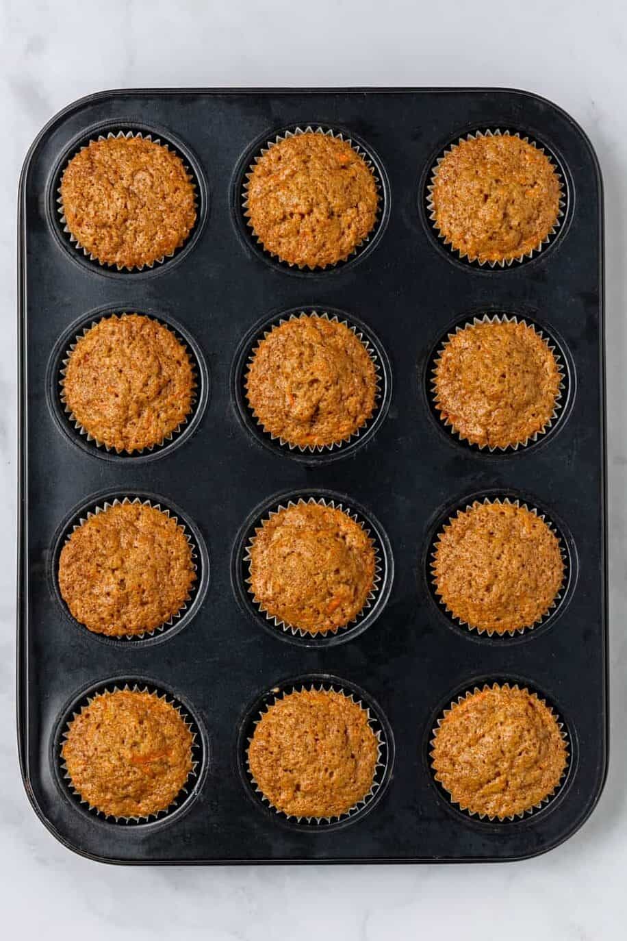 top down image of twelve carrot cake muffins baked in a muffin tin.