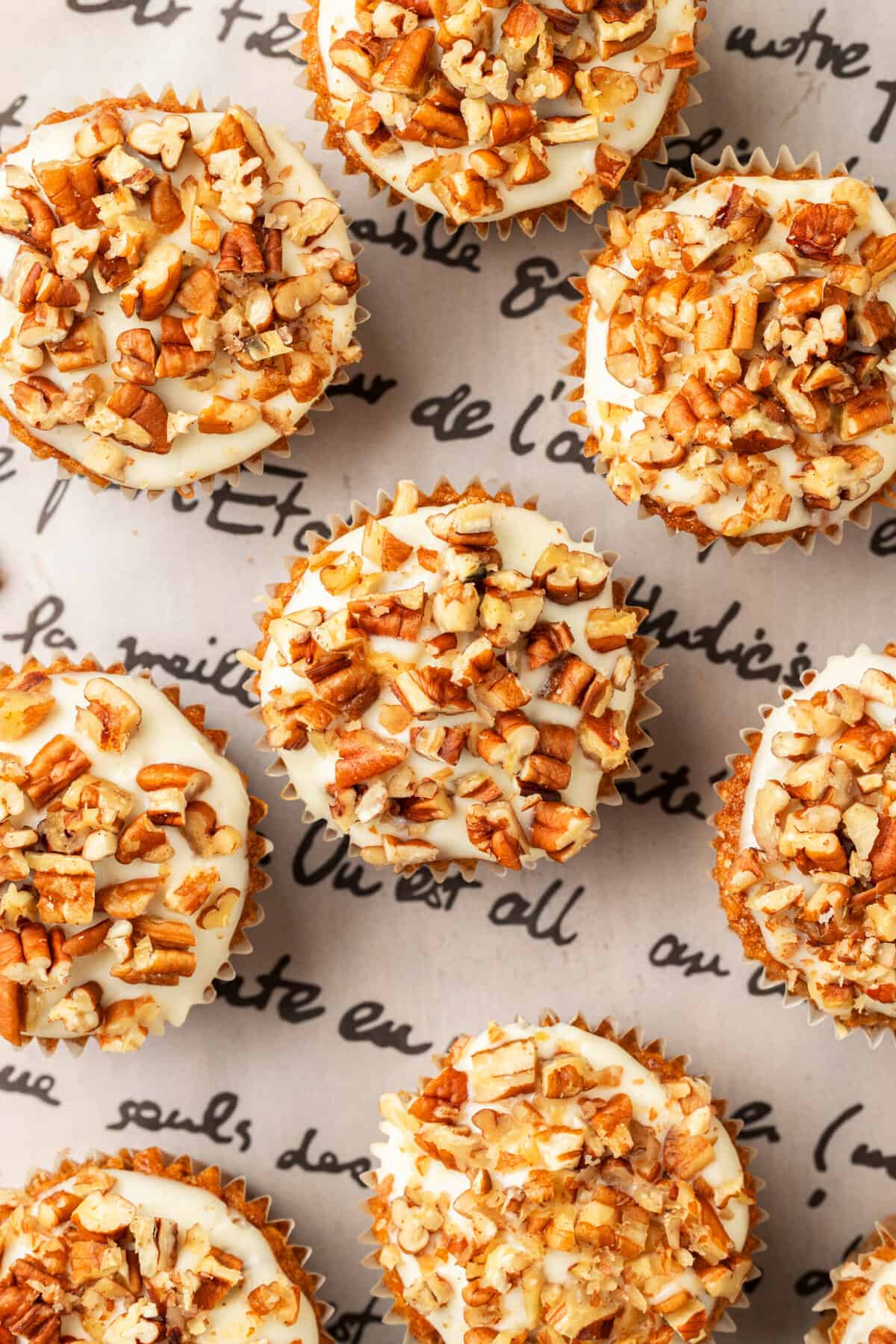 top down image of carrot cake muffins with cream cheese frosting sitting on a patterned surface.