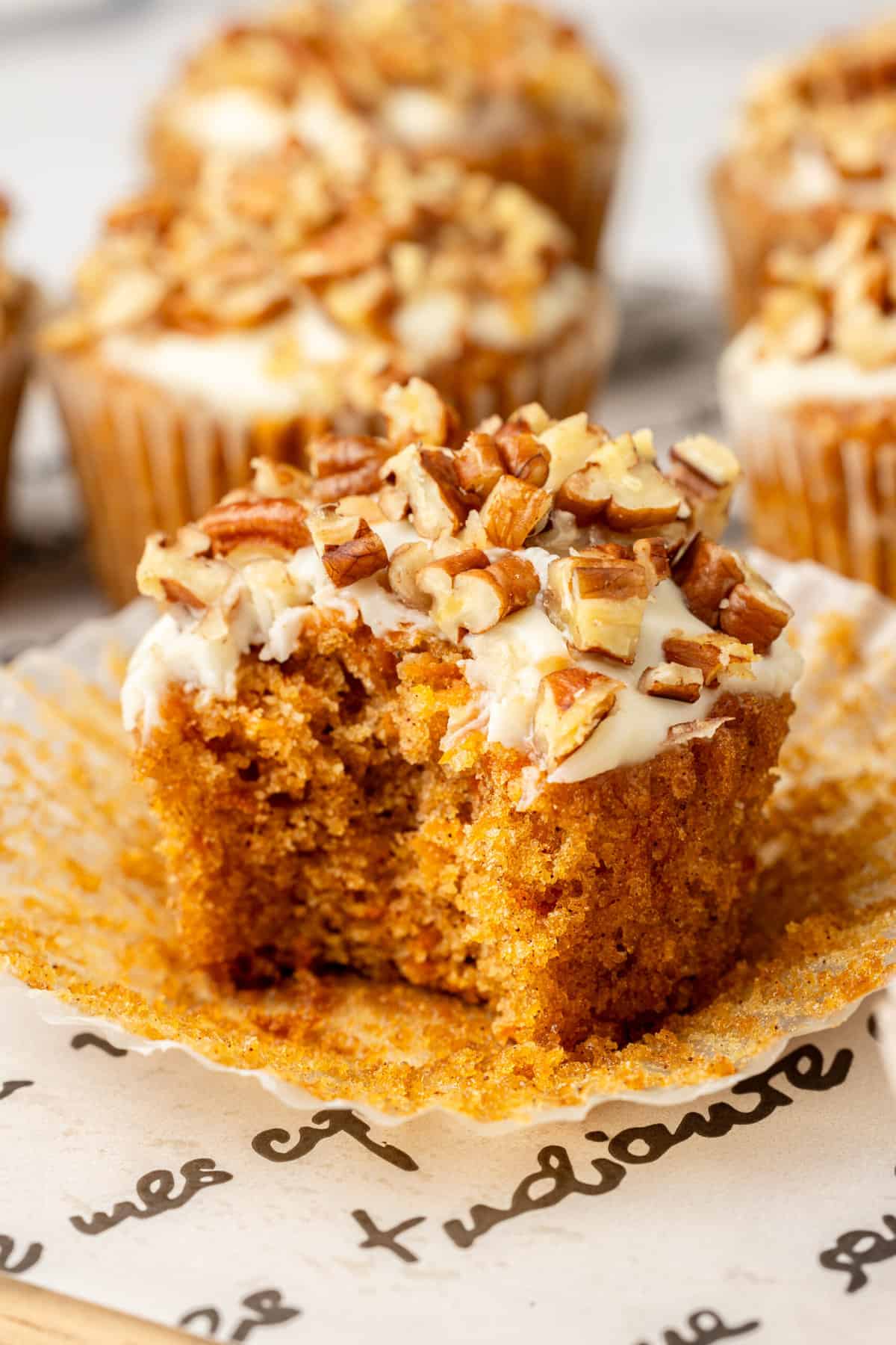 close up image of a carrot cake muffin with cream cheese frosting with a bite taken out of it.