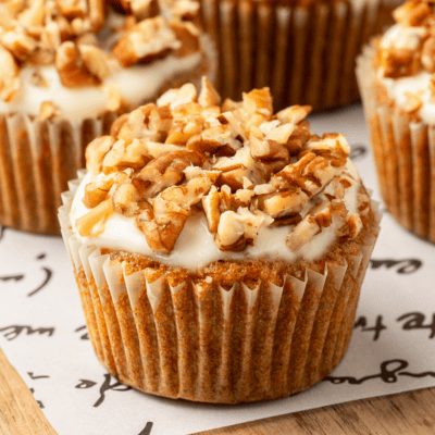 A carrot cake muffin with cream cheese glaze topped with pecans.