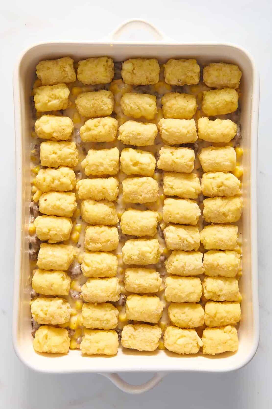 top down image of cowboy casserole prepped ready to bake sitting in a 9x13 inch casserole dish. 
