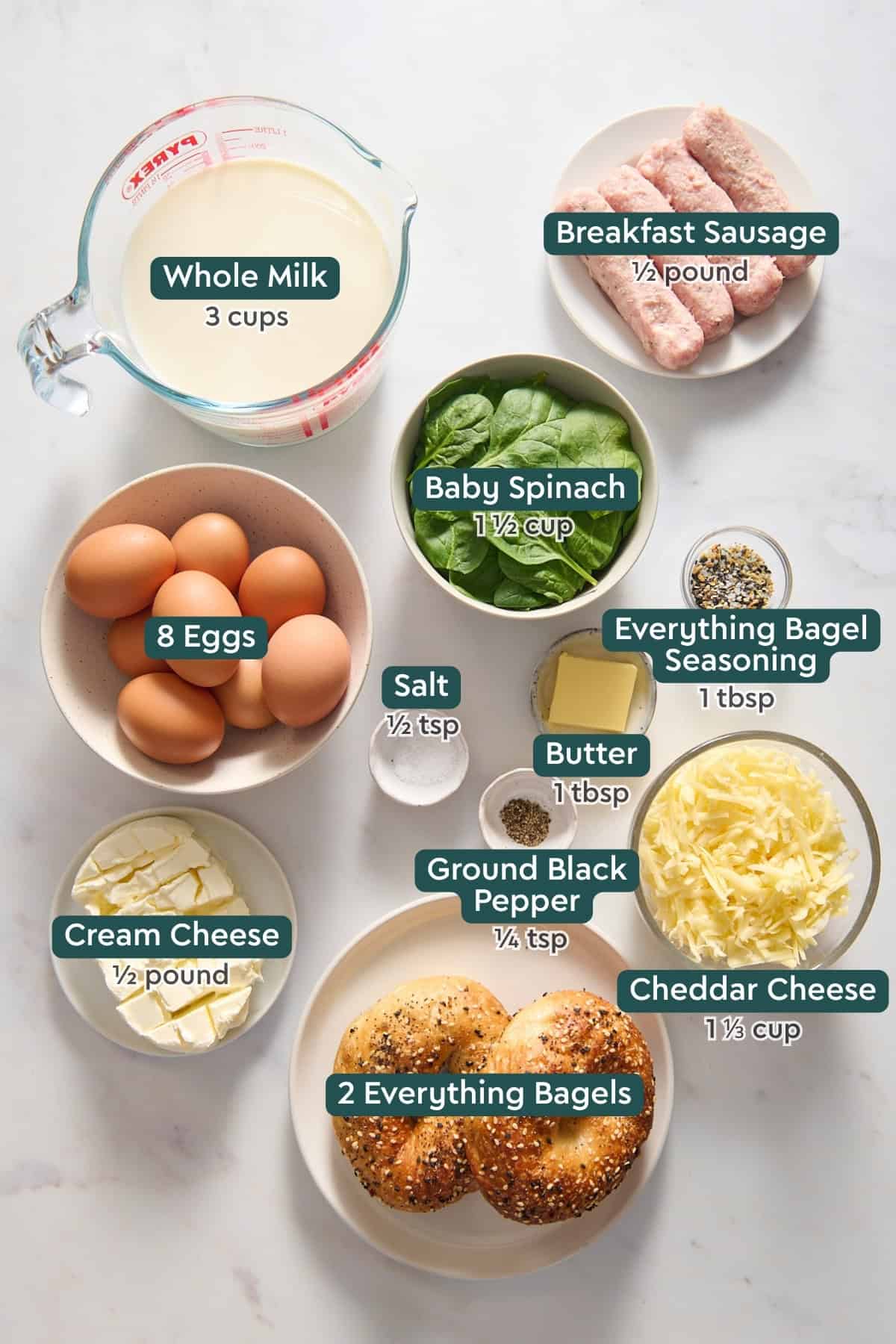 Ingredients for everything bagel breakfast casserole, including sausage, milk, spinach, eggs, seasonings, cheddar, bagels, and cream cheese