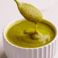 A spoon lifting a scoop of homemade green enchilada sauce from a bowl.