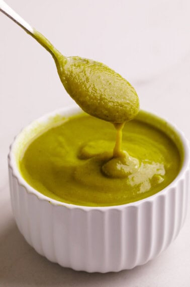 A spoon lifting a scoop of homemade green enchilada sauce from a bowl.