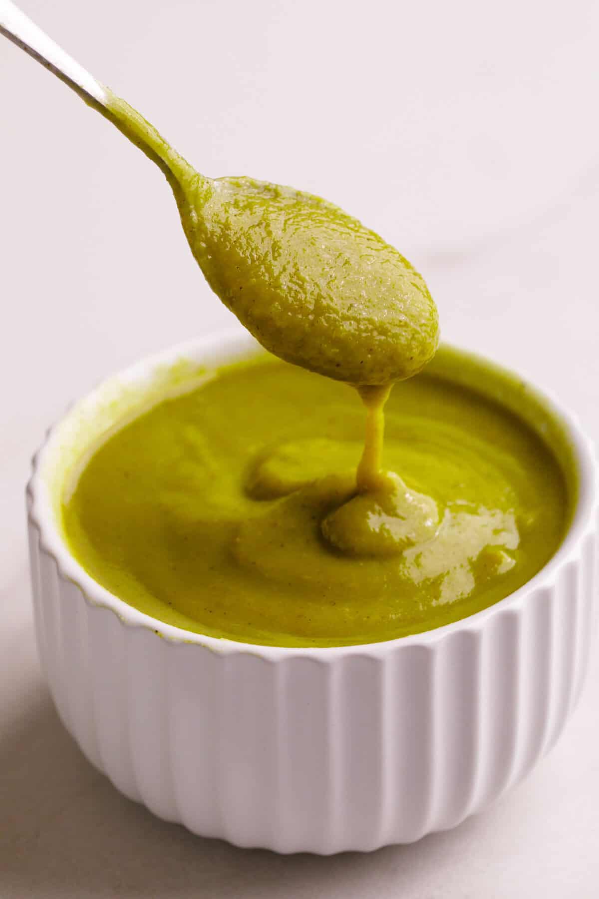 Close-up image of a spoonful, and ramekin with homemade green enchilada sauce.