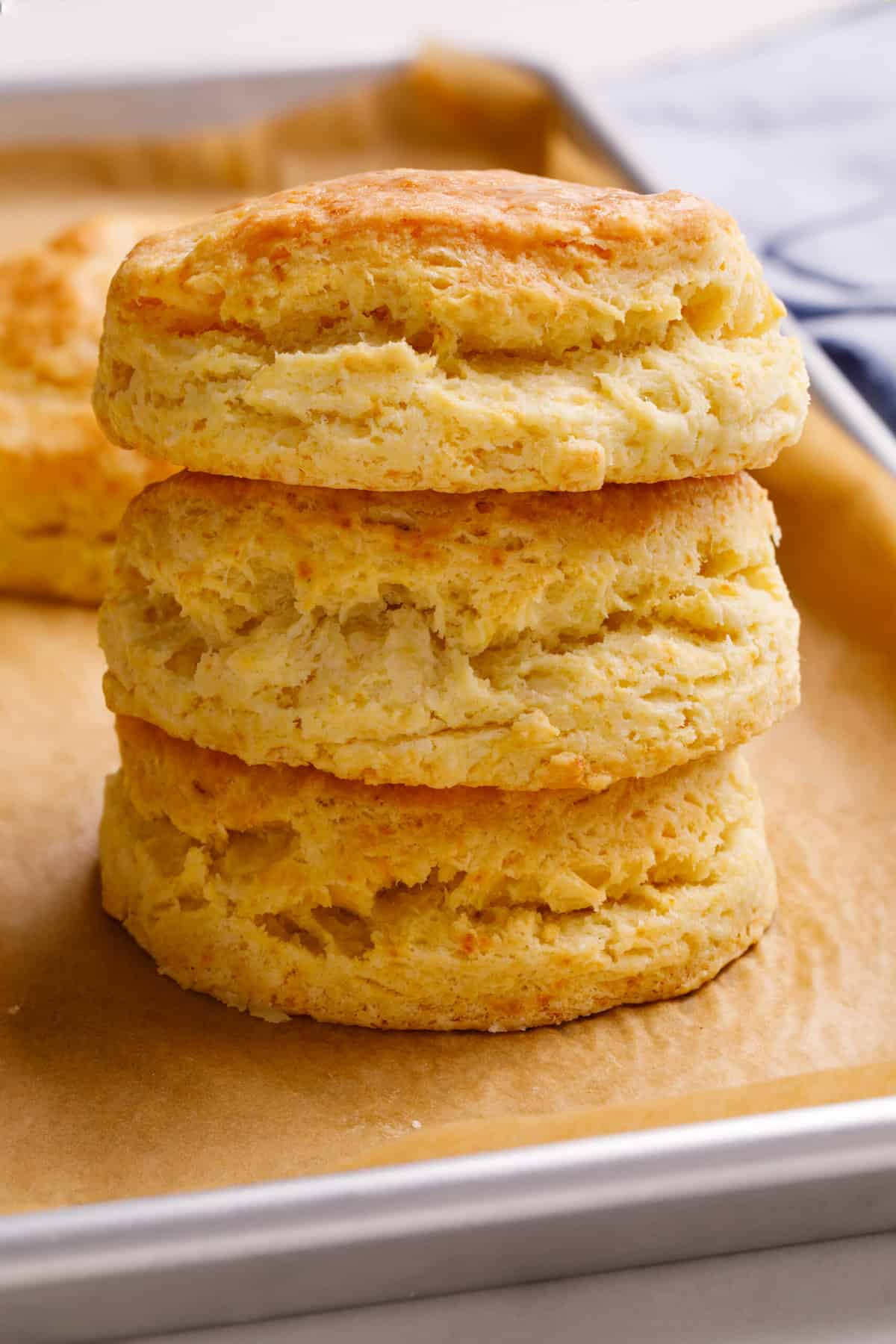 Close-up image of a stack of three homemade Popeyes biscuits sitting on a parchment lined baking tray.