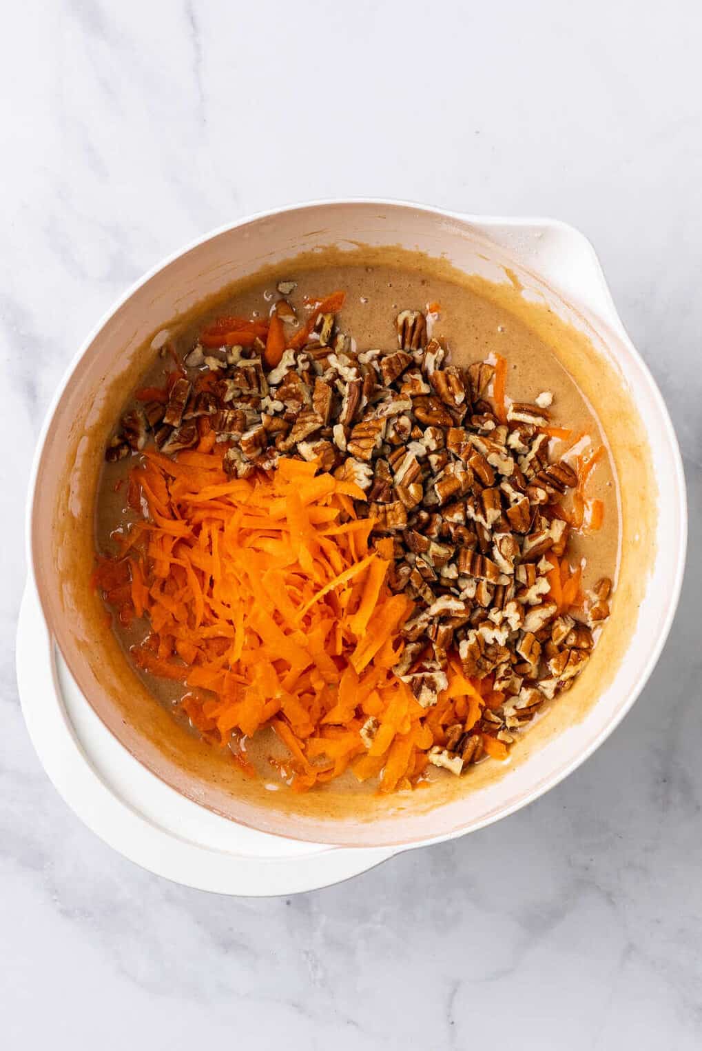 top down image of a white mixing bowl with simple carrot cake batter. 