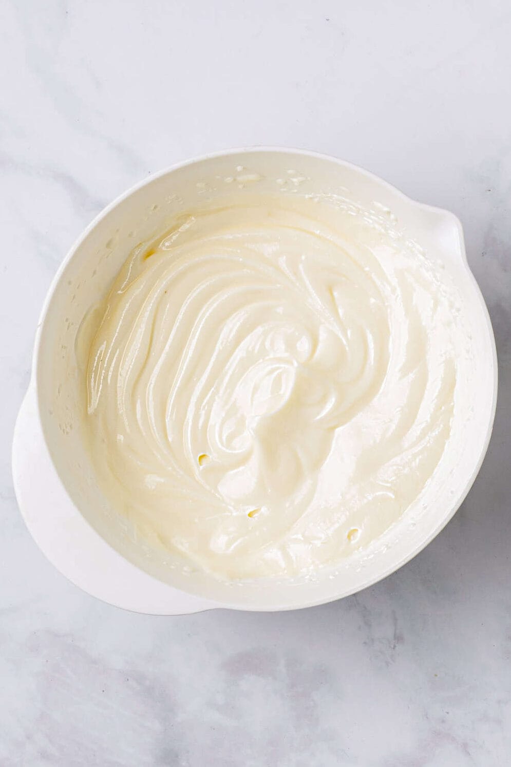 top down image of cream cheese frosting in a white mixing bowl. 