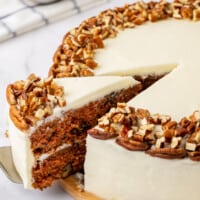 A slice of carrot cake being cut and lifted from a whole cake.