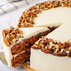 A slice of carrot cake being cut and lifted from a whole cake.