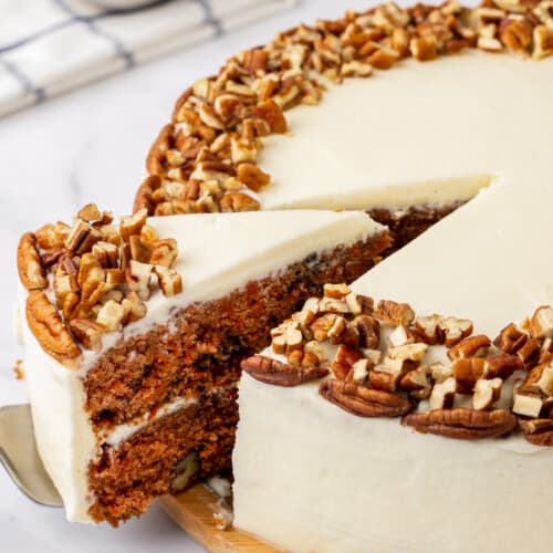 A slice of carrot cake being cut and lifted from a whole cake.