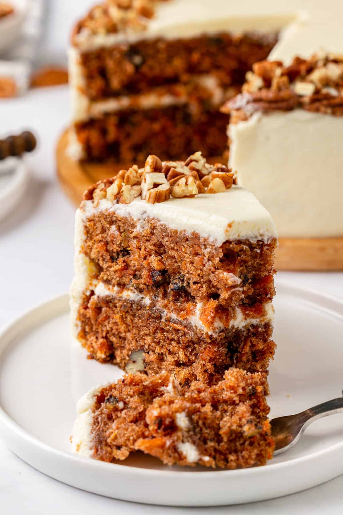 close up image of a slice of simple carrot cake served on a white round plate with a bite taken out of it.