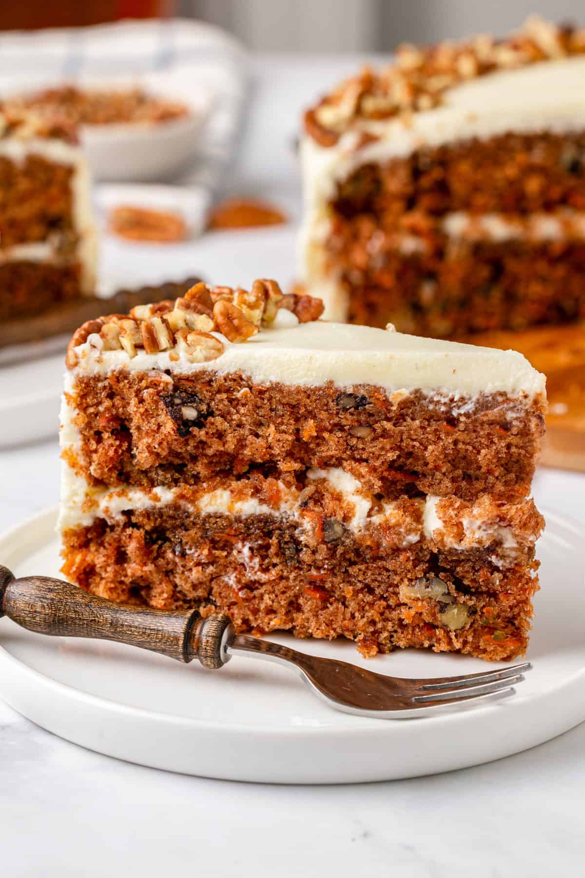 close up image of a slice of simple carrot cake served on a white round plate. 