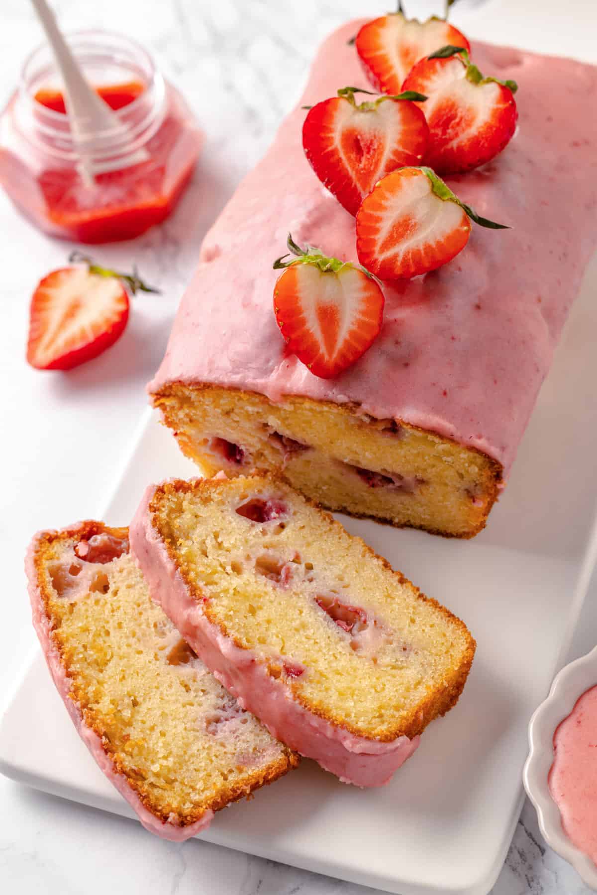 Top image of strawberry pound cake with two slices sitting on a white rectangular plate.