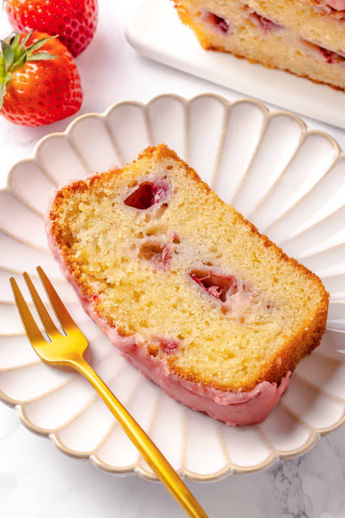 Slice of strawberry poundcake served on a scalloped pink plate with a gold fork.