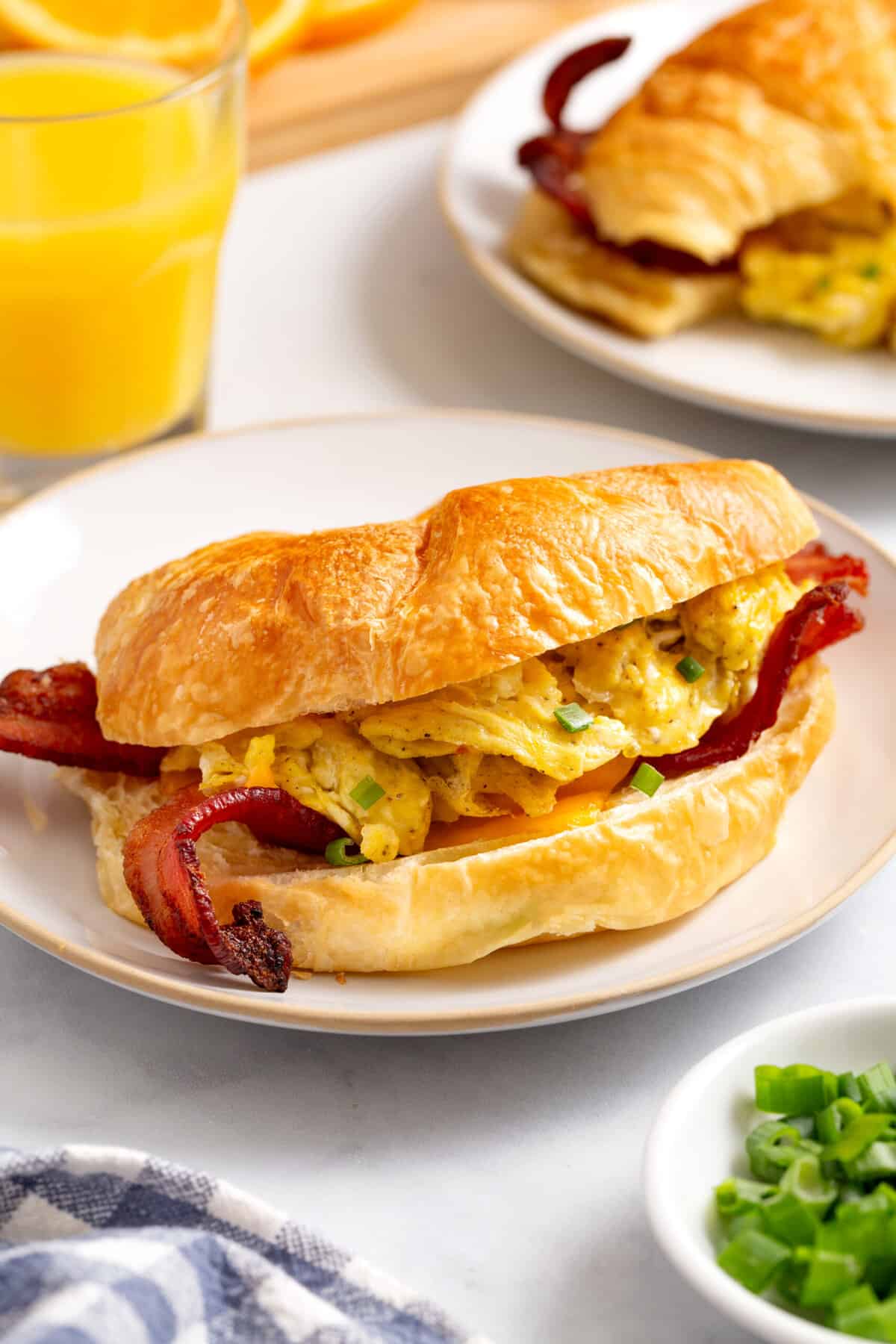 A serving of croissant, breakfast sandwich sitting on a white round plate.