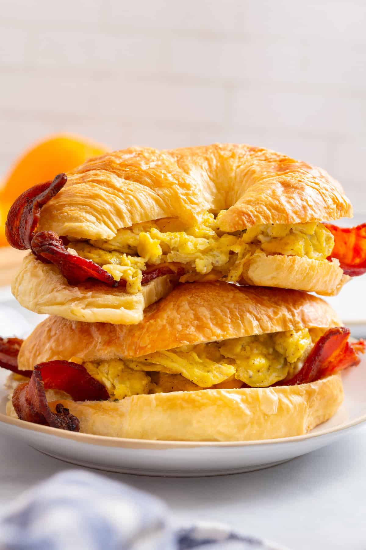 A stack of two croissant breakfast sandwiches, sitting on a white round plate.