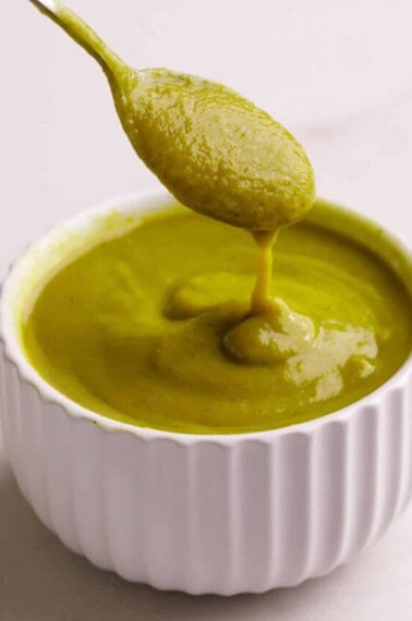 A spoon lifting a scoop of homemade green enchilada sauce from a bowl.