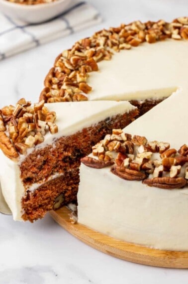 A slice of carrot cake being cut and lifted from a whole cake.
