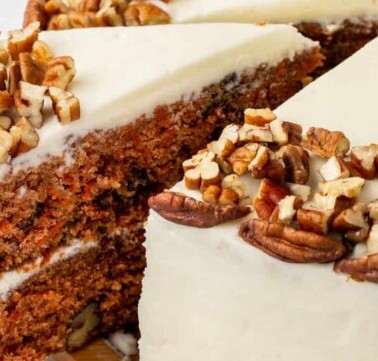 A slice of carrot cake being cut and lifted from a whole cake.