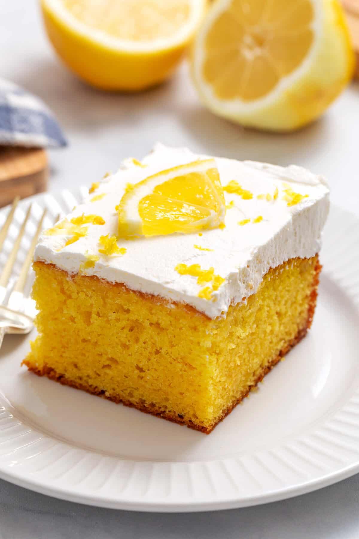Close-up image of a slice of lemon poke cake, sitting on a white round plate.