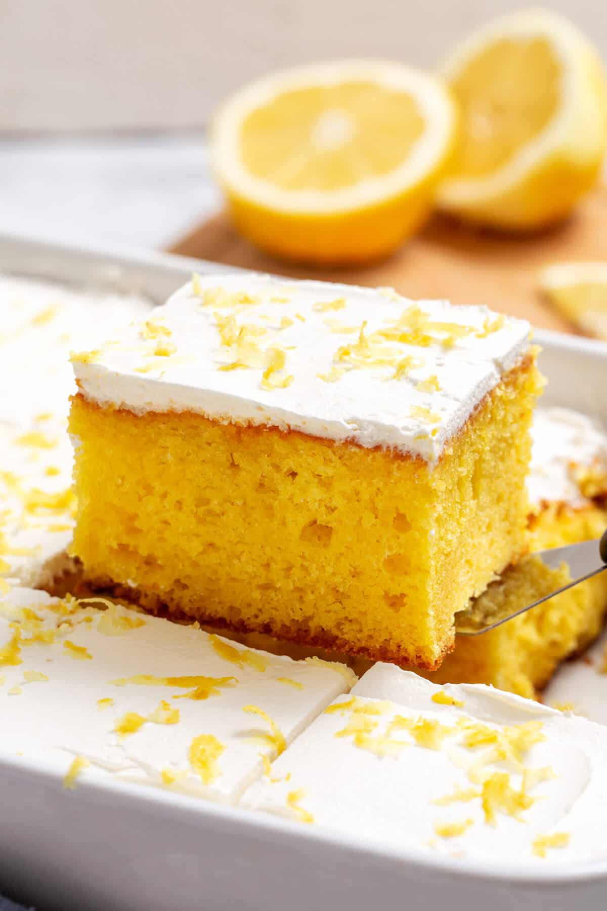 Close-up image of a square slice of lemon poke cake, sitting on a cake spatula.