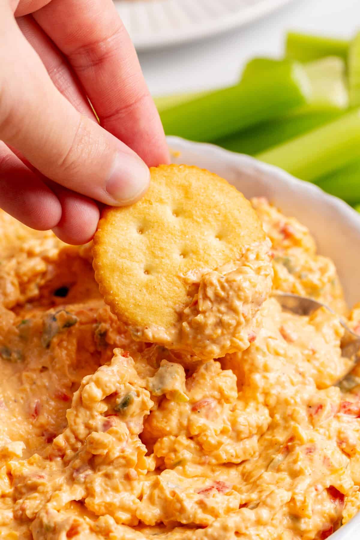 Close up an image of a Ritz cracker, dipping into pimento cheese dip.