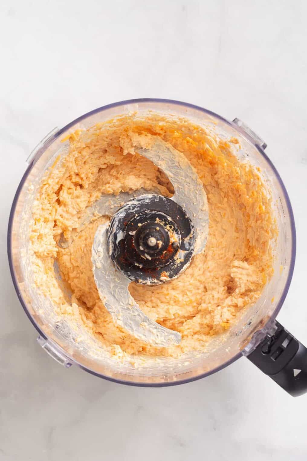 Top down image of a food processor with combined ingredients to make a cheese dip.