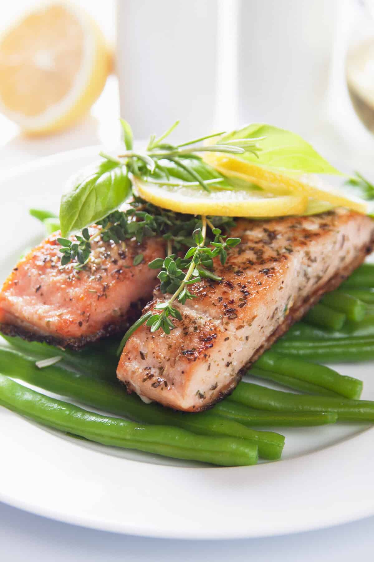 Two pieces of grilled salmon, sitting on a bed of blanched green beans served on a white round plate.