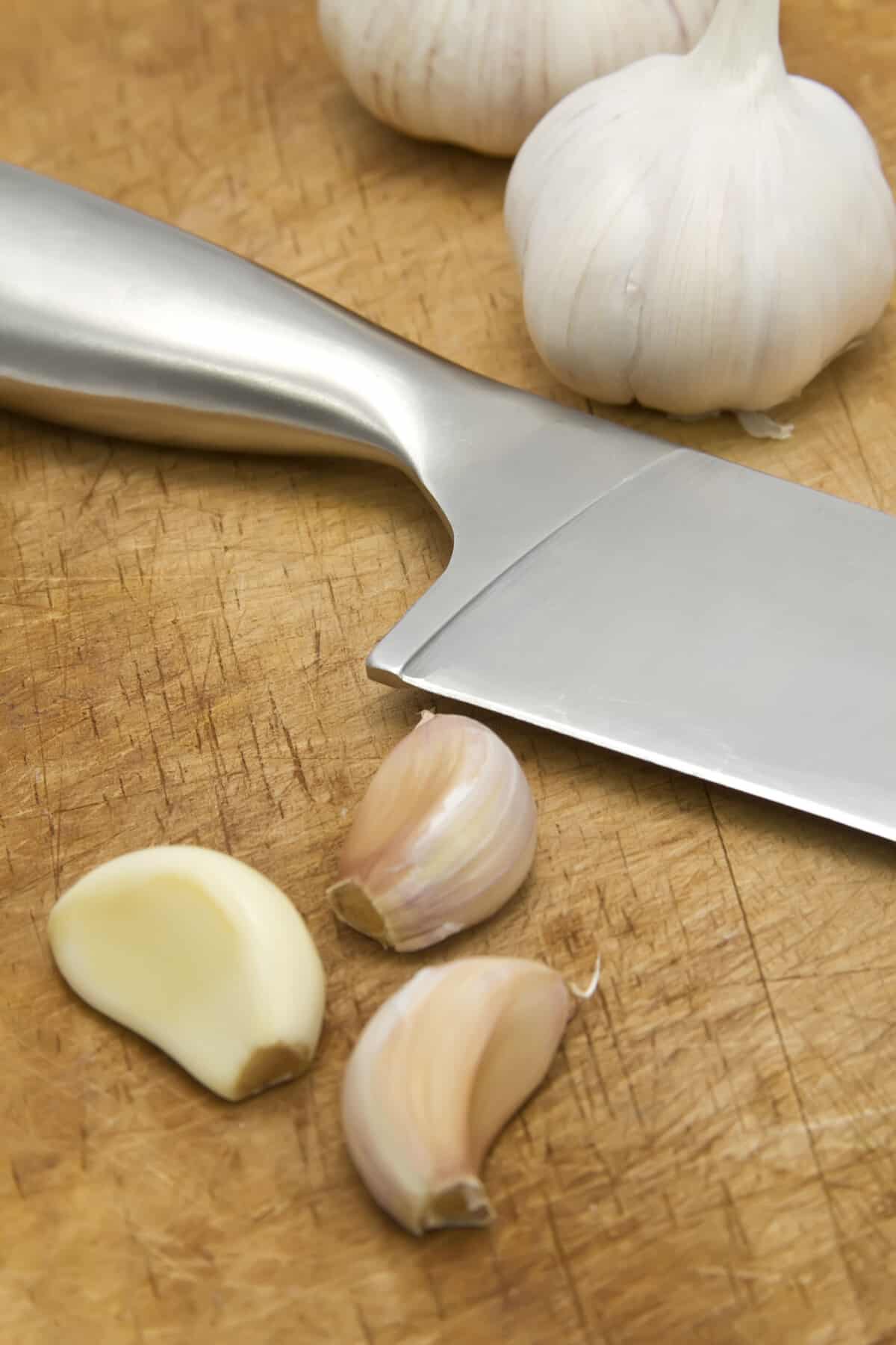 A knife next to garlic bulbs and three cloves of garlic.
