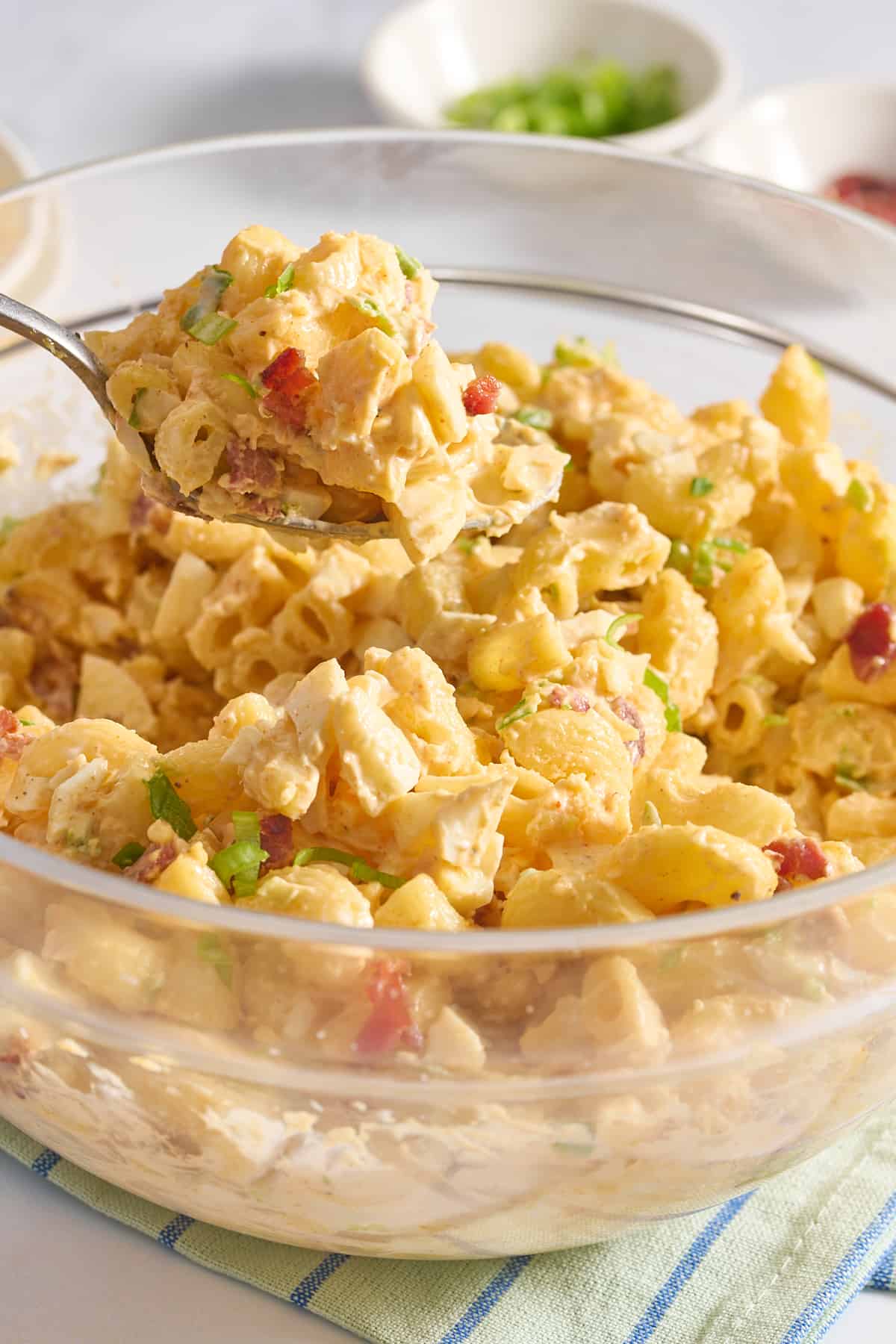 Close-up image of deviled egg, pasta, salad served in a large glass bowl, with a spoonful of the pasta salad.