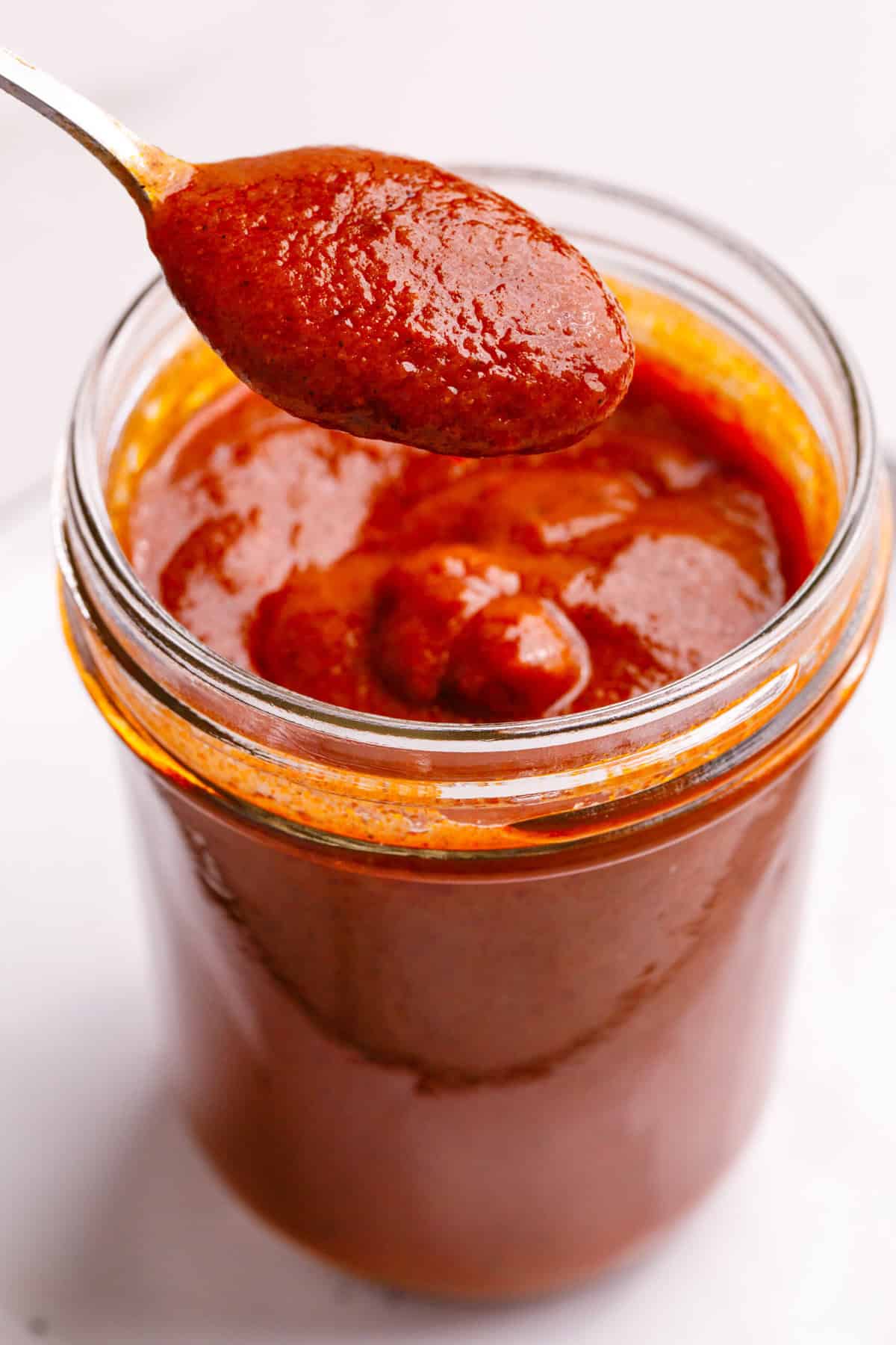 A mason jar of easy red enchilada sauce, and a spoonful of the sauce.