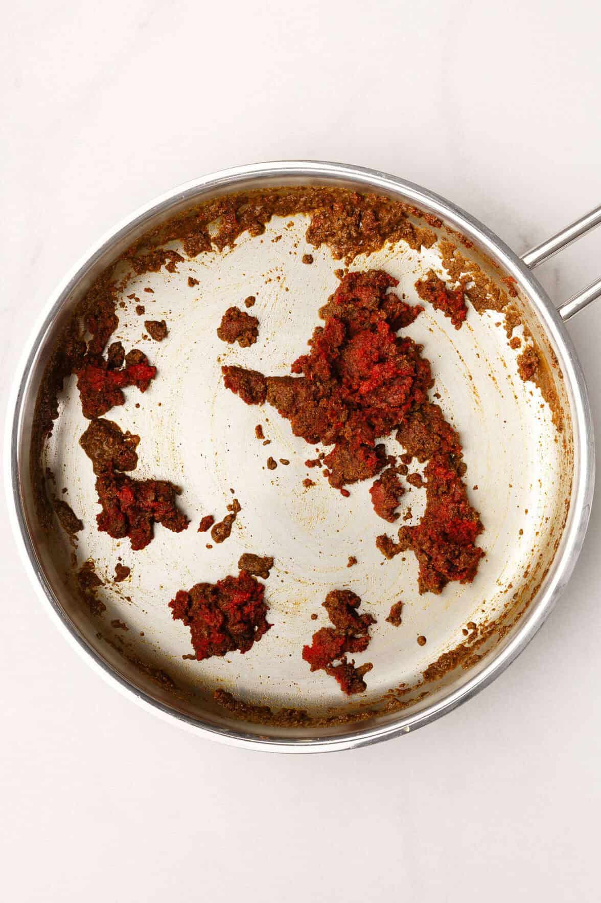 Top down image of a large skillet with tomato paste dry ingredients to make red enchilada sauce.