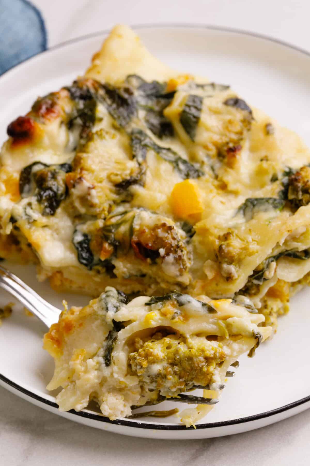 Close up Image of vegetable lasagna with white sauce served on a round plate.