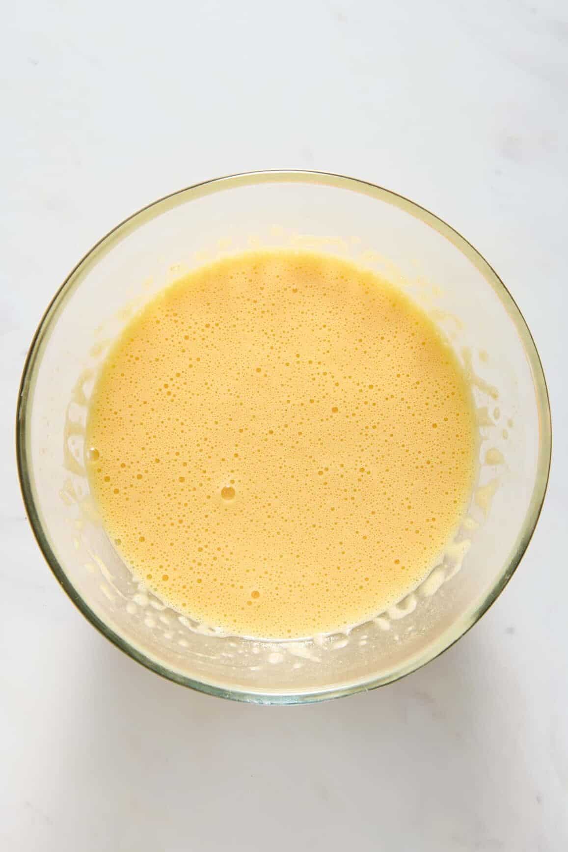 Image of an egg mixture, sitting in a large glass mixing bowl.
